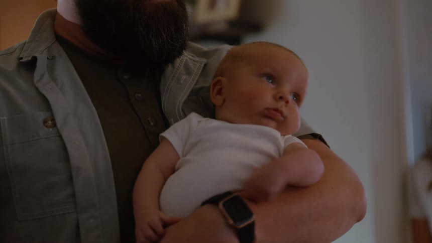 Close-up of a new father lovingly holding his wide-eyed infant son in their home