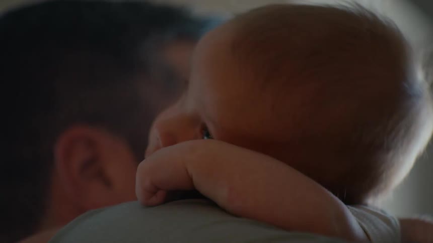 A tender close-up of a newborn baby resting peacefully on its father's shoulder