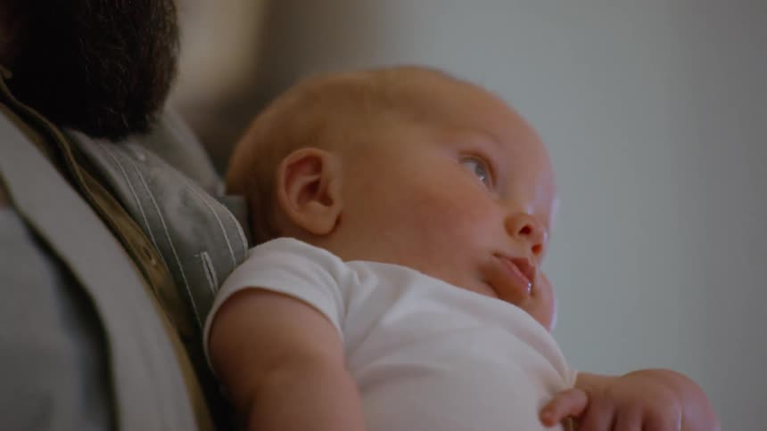 A tender close-up of an adorable newborn baby with blue eyes looking around while being held in their parent's arms