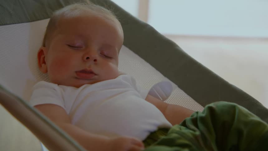 A close-up shot of a sweet newborn baby sleeping peacefully in a bouncer