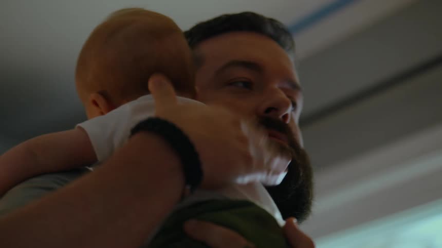A tender close-up of a bearded father gently patting his baby's back while holding him over his shoulder