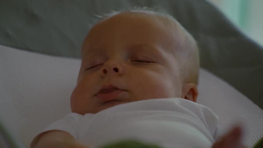 An adorable newborn baby with chubby cheeks sleeps peacefully in their bouncer