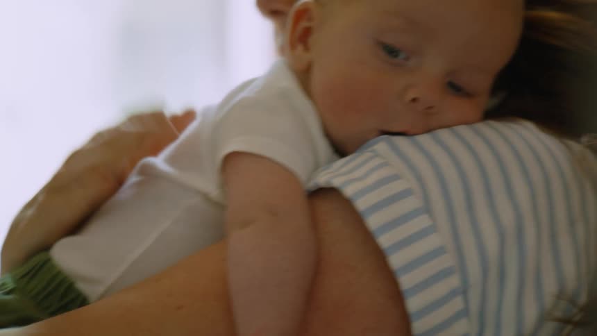 A loving mother gently pats her newborn baby's back as he rests sleepily on her shoulder