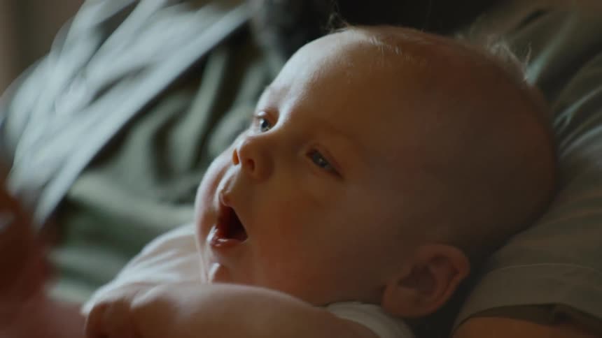 A close-up shot of a sleepy newborn baby yawning while being held by their parent
