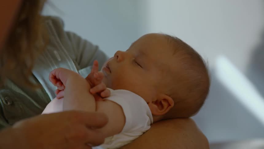 A loving mother gently cradles her sleeping newborn baby in her arms in a softly lit room
