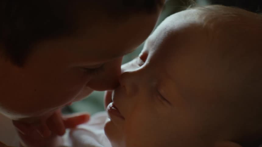 An older brother lovingly gives his newborn baby sibling an Eskimo kiss in a tender close-up