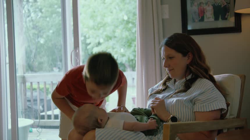 A loving older brother gently kisses his newborn sibling's belly as his mother watches from her chair