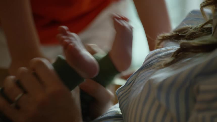 A mother's hands gently hold her newborn baby's tiny kicking feet in an intimate family moment