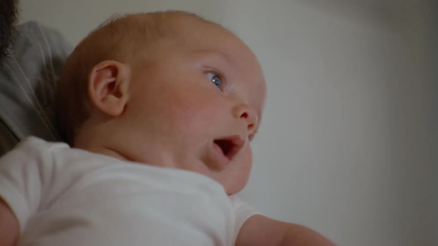 A tender close-up of a father holding his newborn baby, with the camera slowly focusing on the infant's curious, wide-eyed expression