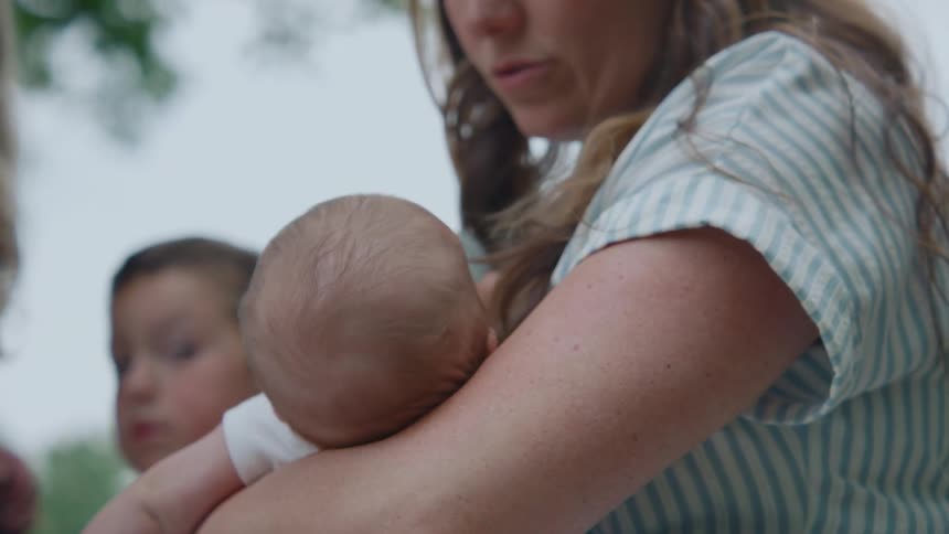A loving mother holds her newborn baby close in her arms while outdoors