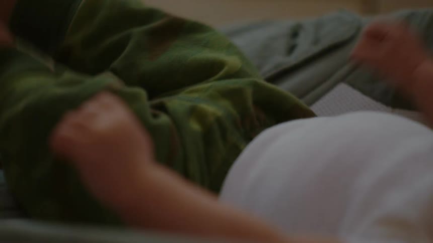 Soft-focus close-up of a newborn infant in green pants waving their hands and kicking their feet