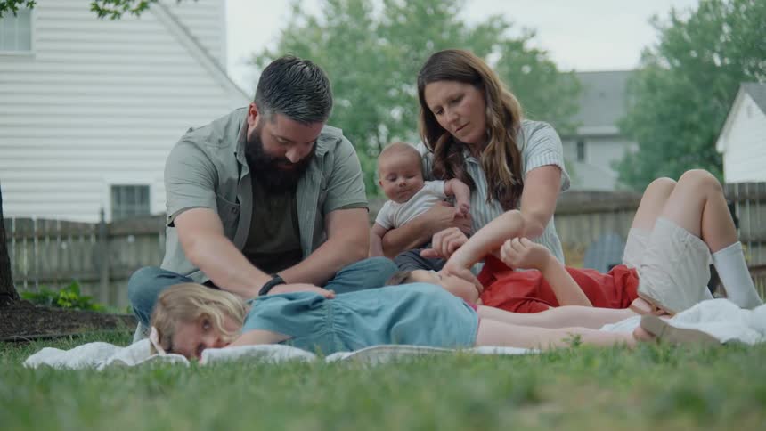 A gentle family of five relaxes on a blanket in their green backyard on a summer day