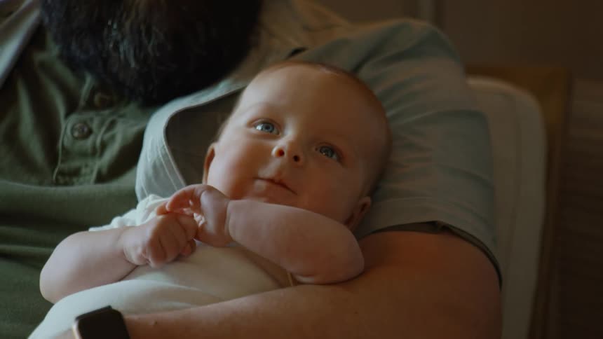 A happy, blue-eyed baby smiles while being held safely in their father's arms
