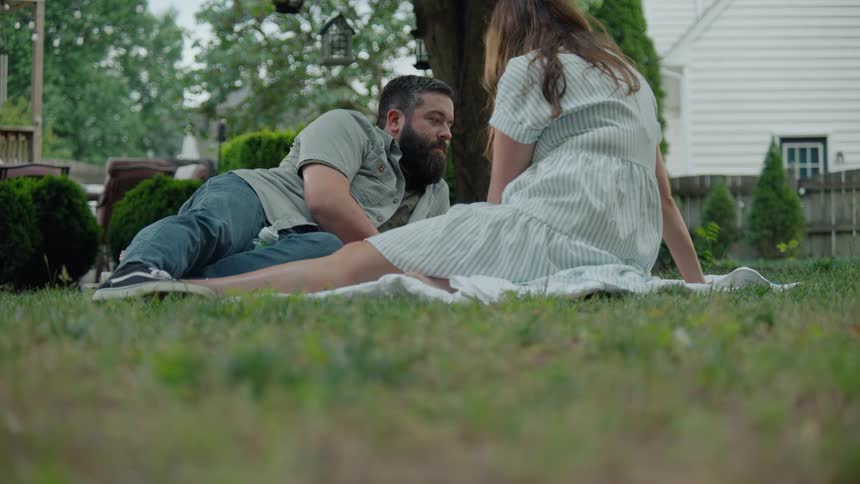 An intimate low-angle shot of a couple relaxing on a blanket in their backyard, talking and enjoying each other's company