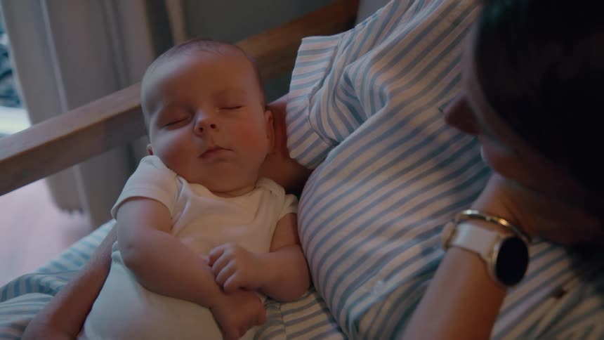 Close up of a peaceful newborn baby sleeping in its mother's arms as she watches over them