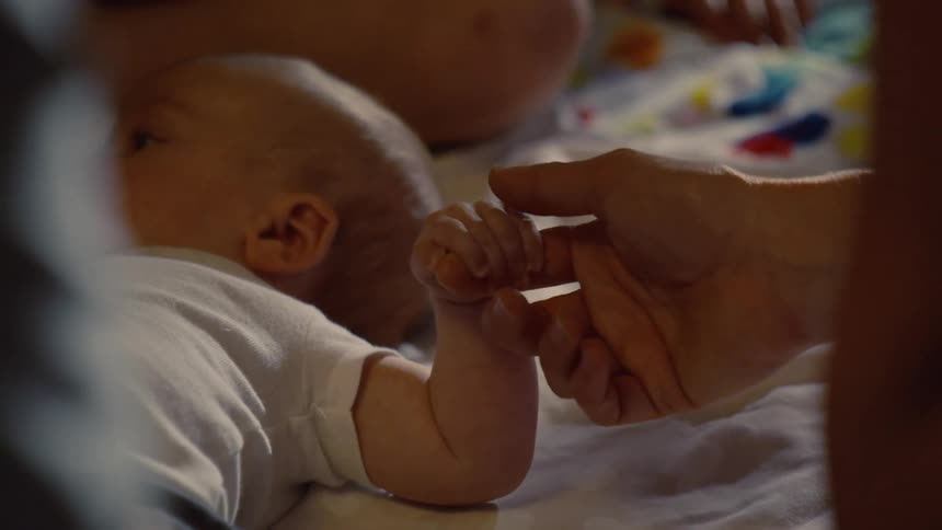 A newborn baby gently grips an adult's finger in a tender moment of connection