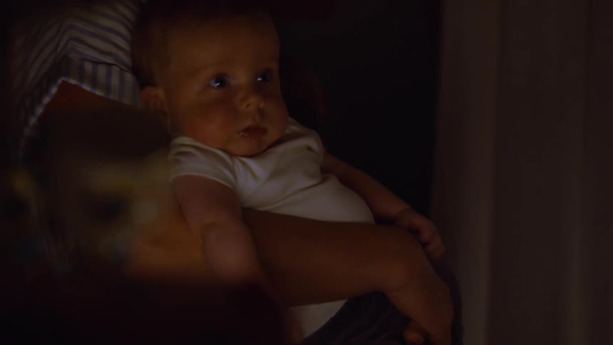A curious newborn baby with big blue eyes is held lovingly in its mother's arms in a warm, dark room