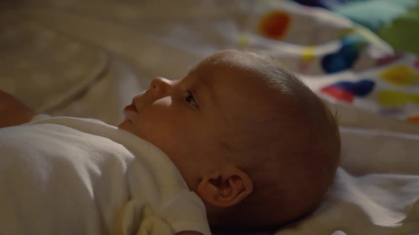 A serene newborn baby rests quietly in bed, gazing upward in a moment of calm