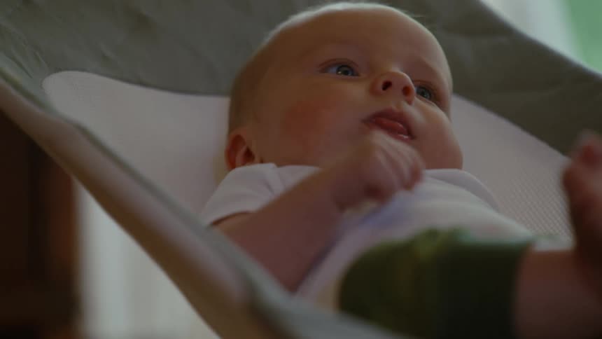 A close-up shot of an adorable newborn baby yawning and then looking around contentedly while lying in a baby bouncer