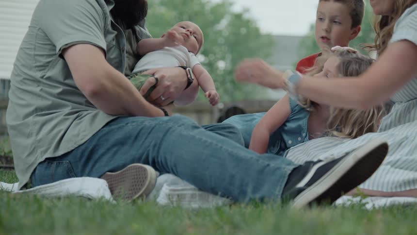 A beautiful family of five spends a loving moment together on a blanket in the backyard with their newborn baby