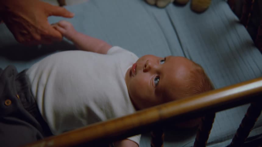 A tender moment as a parent gently holds the hand of their newborn baby lying peacefully in a wooden crib