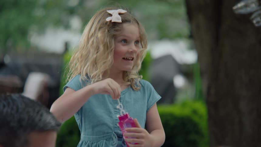 A young boy and girl laugh with joy as they blow soap bubbles in a lush backyard in slow motion