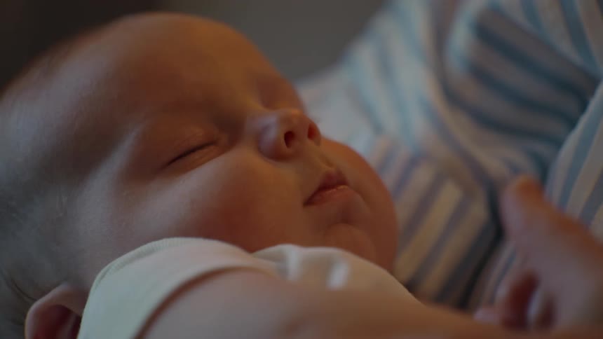 A loving mother gently soothes her sleeping newborn baby in a warm, cozy embrace