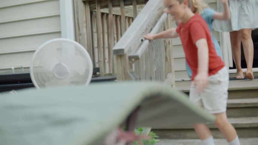 Happy siblings energetically run out the back door and down the steps of their home in slow motion