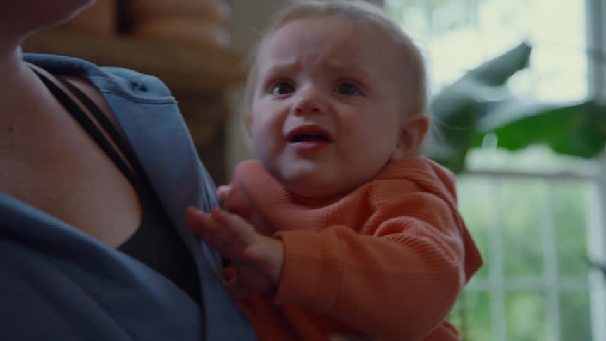 A close-up of a baby's face as it goes from laughing joyfully to crying sadly while held in its mother's arms