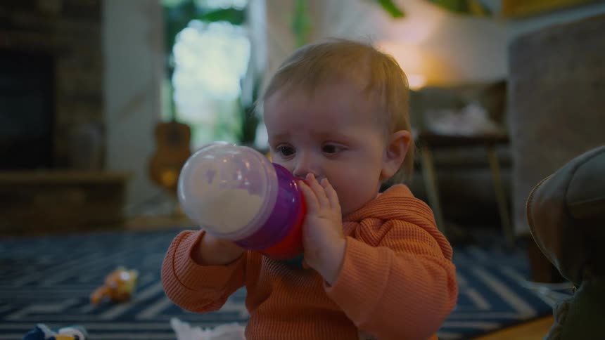 A close-up shot of a baby sitting on the floor drinking from a bottle
