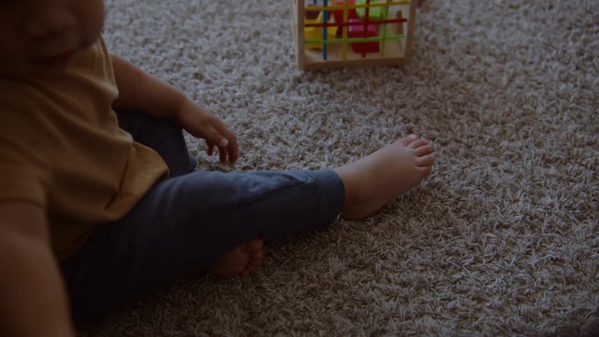 A small child sits on a cozy carpet and plays with a little blue ball in a softly lit room