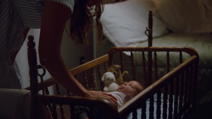 A loving mother gently places a pacifier in her newborn baby's mouth as they lie in a wooden cradle at night
