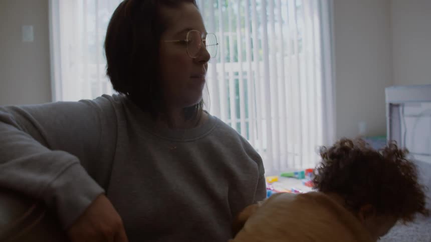 A loving mother comforts and holds her toddler in their bright, toy-filled living room