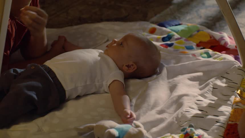 A young boy lovingly kisses his infant sibling as they lay together on a colorful playmat indoors
