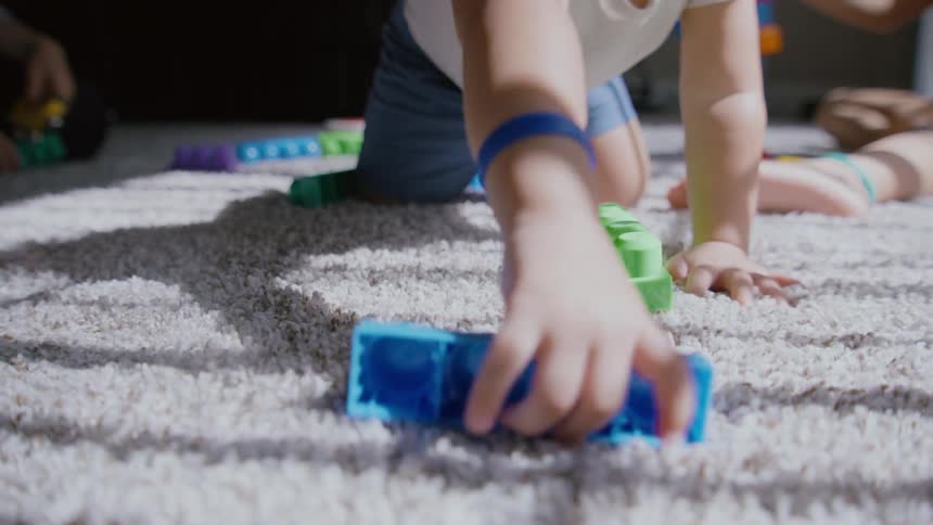 A child in slow motion reaches for a colorful toy block while playing on a sunlit carpet