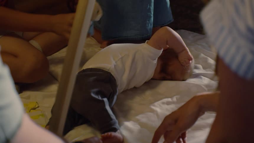 A newborn baby lies on a playmat on the floor while being lovingly entertained by its mother and siblings