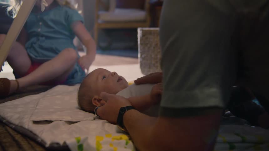 Heartwarming family moment captures a father lovingly bonding with his newborn baby on the floor as his daughter plays in the background