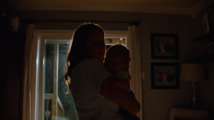A loving mother holds her baby close in her arms, silhouetted in a dimly lit room at night