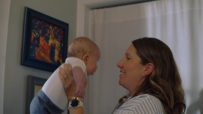 A happy mother lifts her newborn baby into the air, smiling and giving loving kisses in a sunlit room