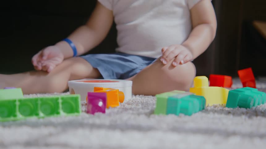 A close up of a toddler and sibling playing together with colorful building blocks on a soft white carpet