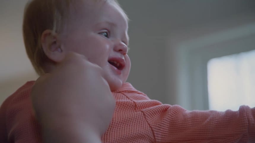 A parent gently holds their crying baby's face as the infant's expression changes to a happy smile in slow motion