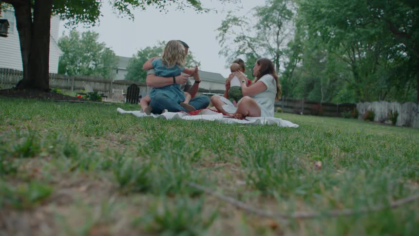 A beautiful family of five enjoys a quiet afternoon together, sitting on a blanket in their lush green backyard