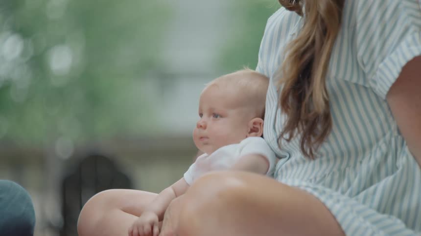 A mother gently holds her newborn baby in her lap while they sit together outdoors