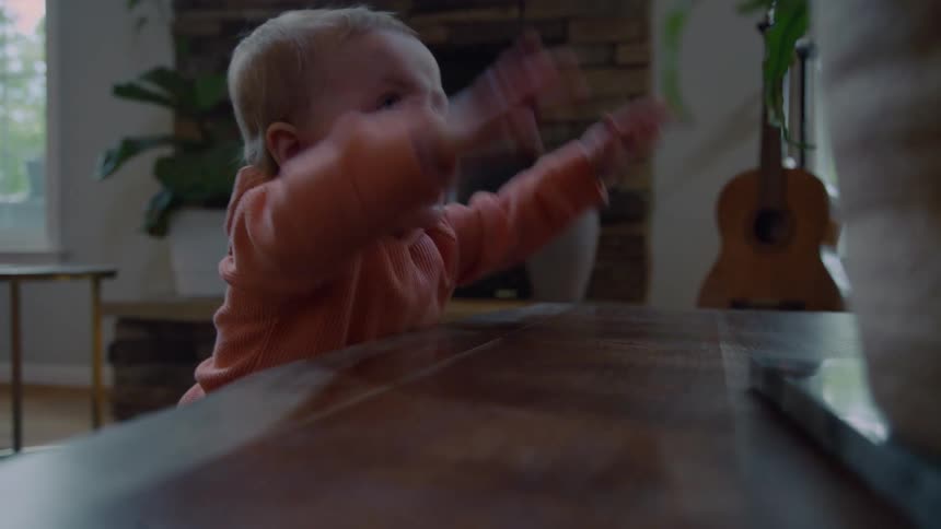 A cute baby playing hide and seek pops up laughing and then gets excited, slapping their hands on a wooden table