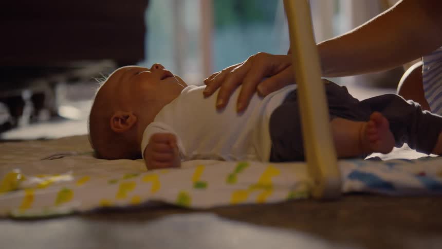 A mother gently soothes her crying newborn baby with a toy and a tender touch on a play mat