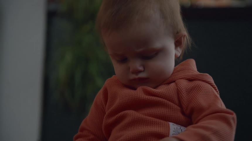 An adorable baby boy with red hair looks pensive and then breaks into a wide, happy smile