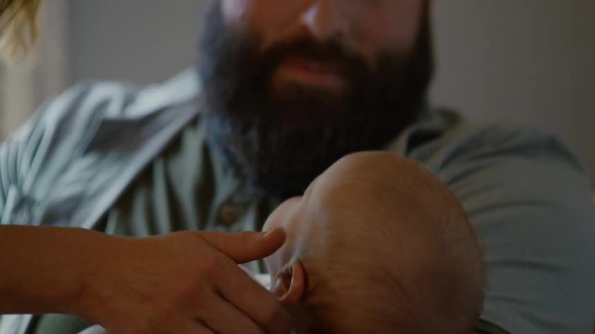 A loving mother smiles as she and her husband cradle their newborn baby in a quiet, tender moment at home