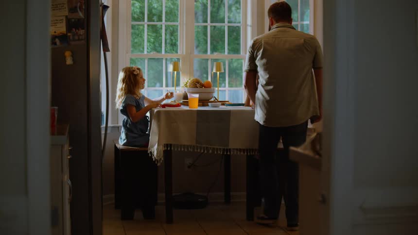 A father walks into the dining room to join his young son and daughter for a meal at the table