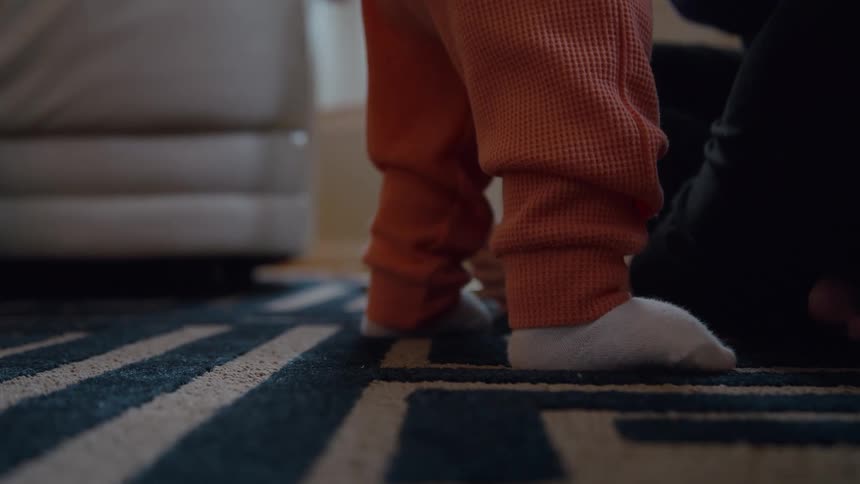 A close-up shot of a baby's tiny feet in socks as they wobble and learn to stand on a patterned rug