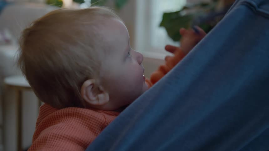 A close-up shot shows a teething baby chewing on the drawstring of their parent's blue hoodie